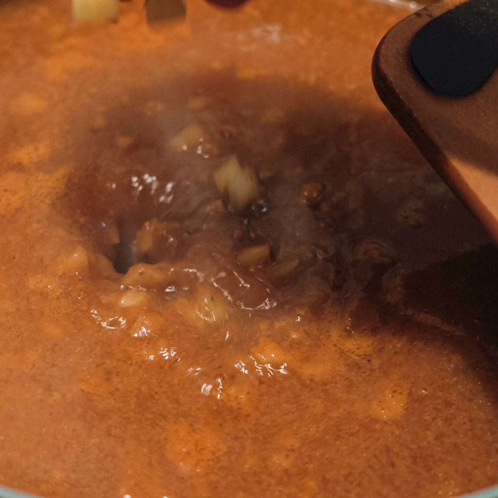 Patatas crudas cortadas en dados cayendo en una base de sopa sabrosa y burbujeante de color naranja con vapor subiendo de la olla.