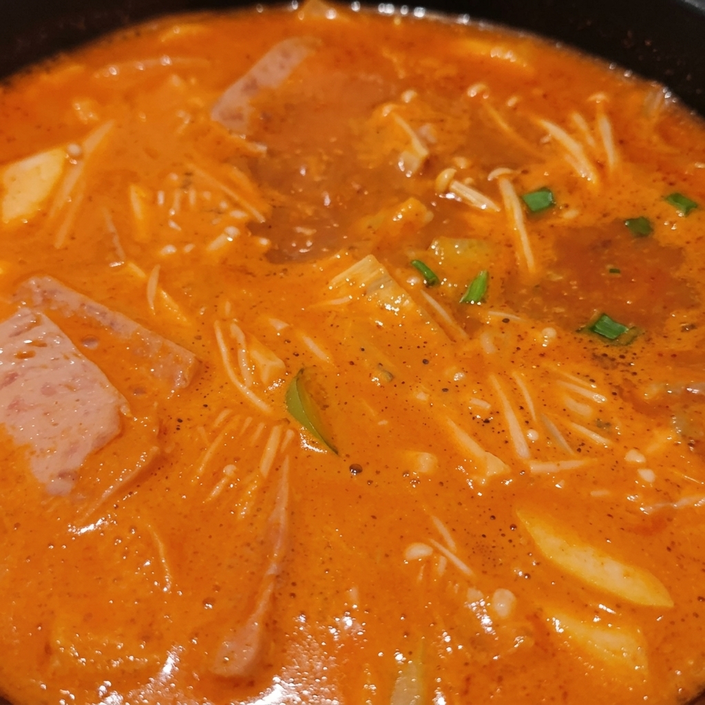 Un estofado coreano burbujeante repleto de setas enoki, láminas de carne, cebolleta verde y tofu sumergidos en un rico caldo naranja.