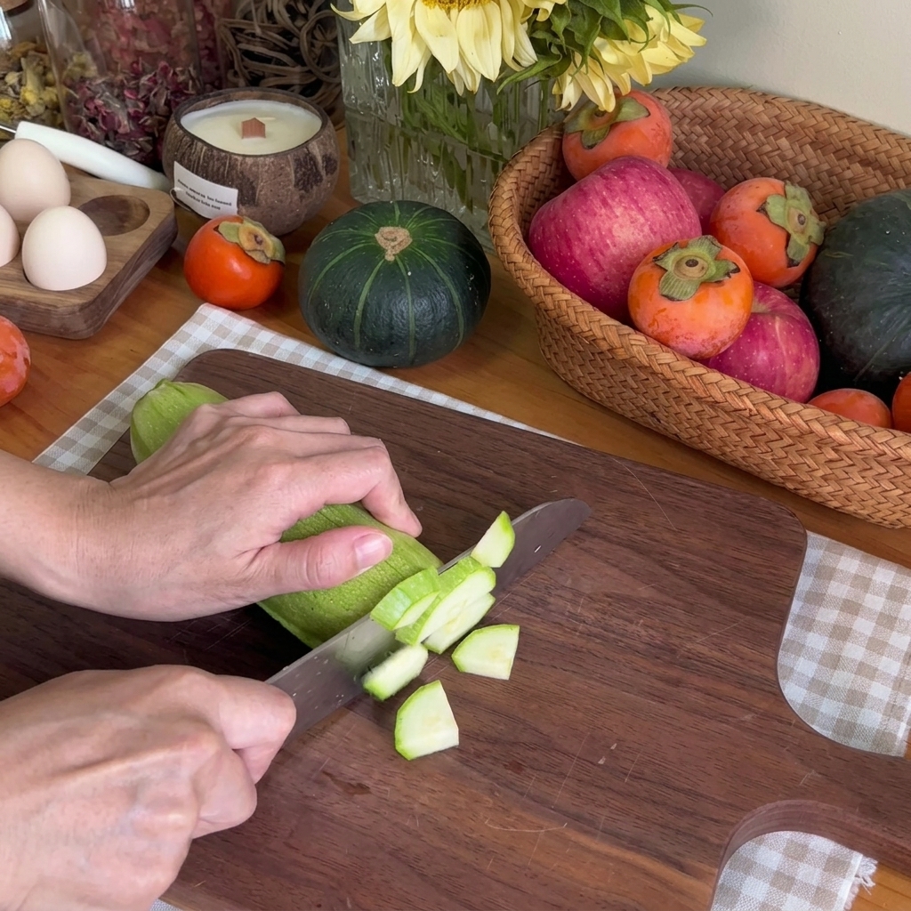 Primer plano de unas manos usando un cuchillo de chef para cortar un calabacín verde en trozos pequeños sobre una tabla de picar de madera.