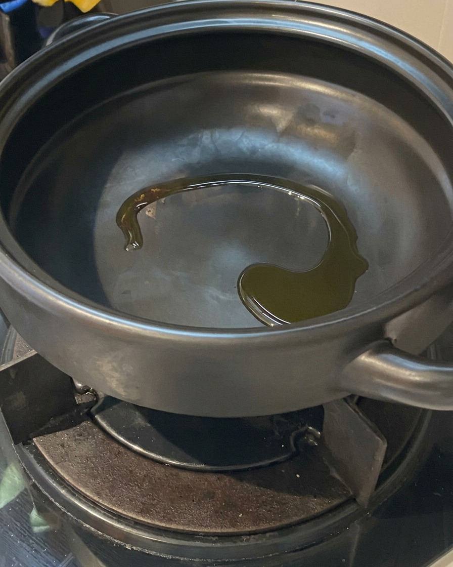 Aceite de cocina brillando en el fondo de una olla de barro negra caliente sobre un quemador de estufa a gas.