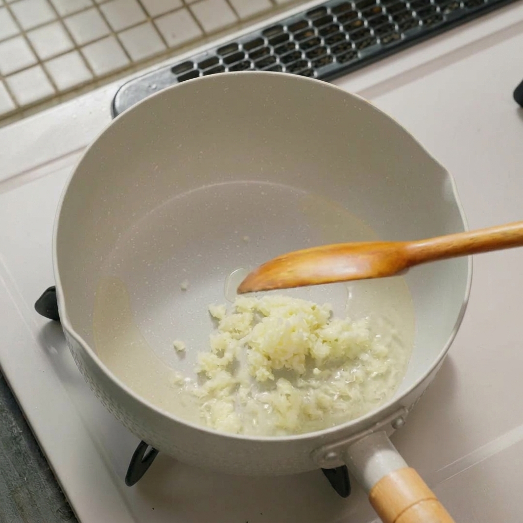 Ajo finamente picado y cebolleta chisporroteando en aceite en el fondo de una olla con una cuchara de madera.