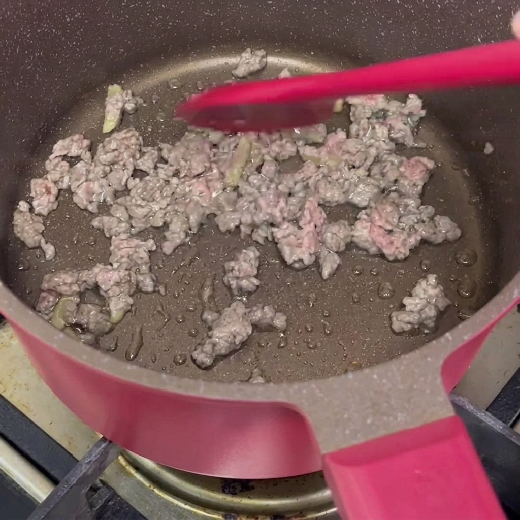 Ternera picada marinada siendo salteada con una espátula de silicona roja en una olla rosa.