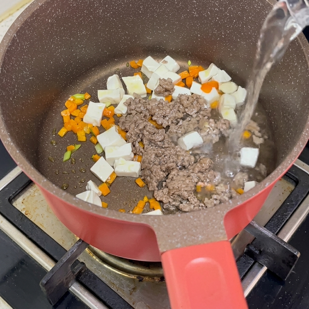 Cubos de tofu, ternera picada y zanahorias siendo cubiertos con agua hirviendo en una olla.