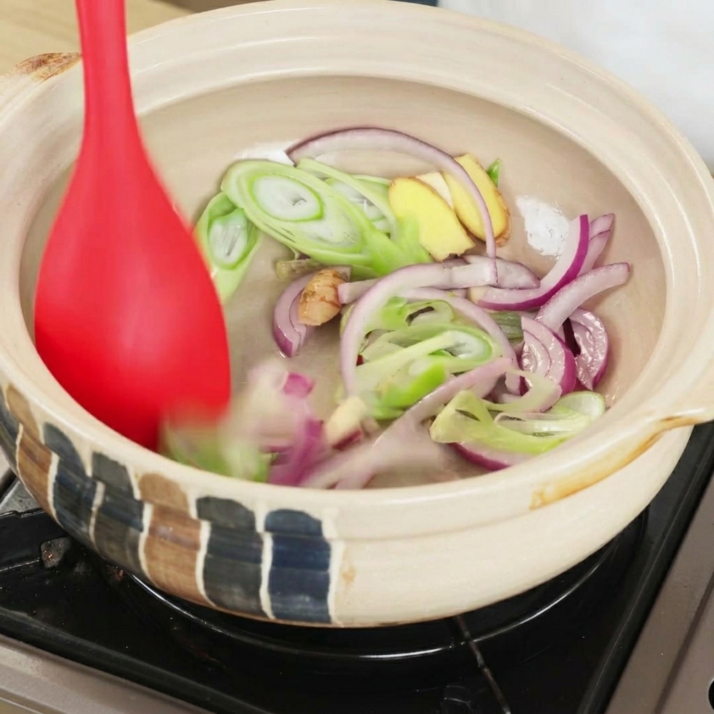 Espátula removiendo los ingredientes aromáticos en la cazuela.