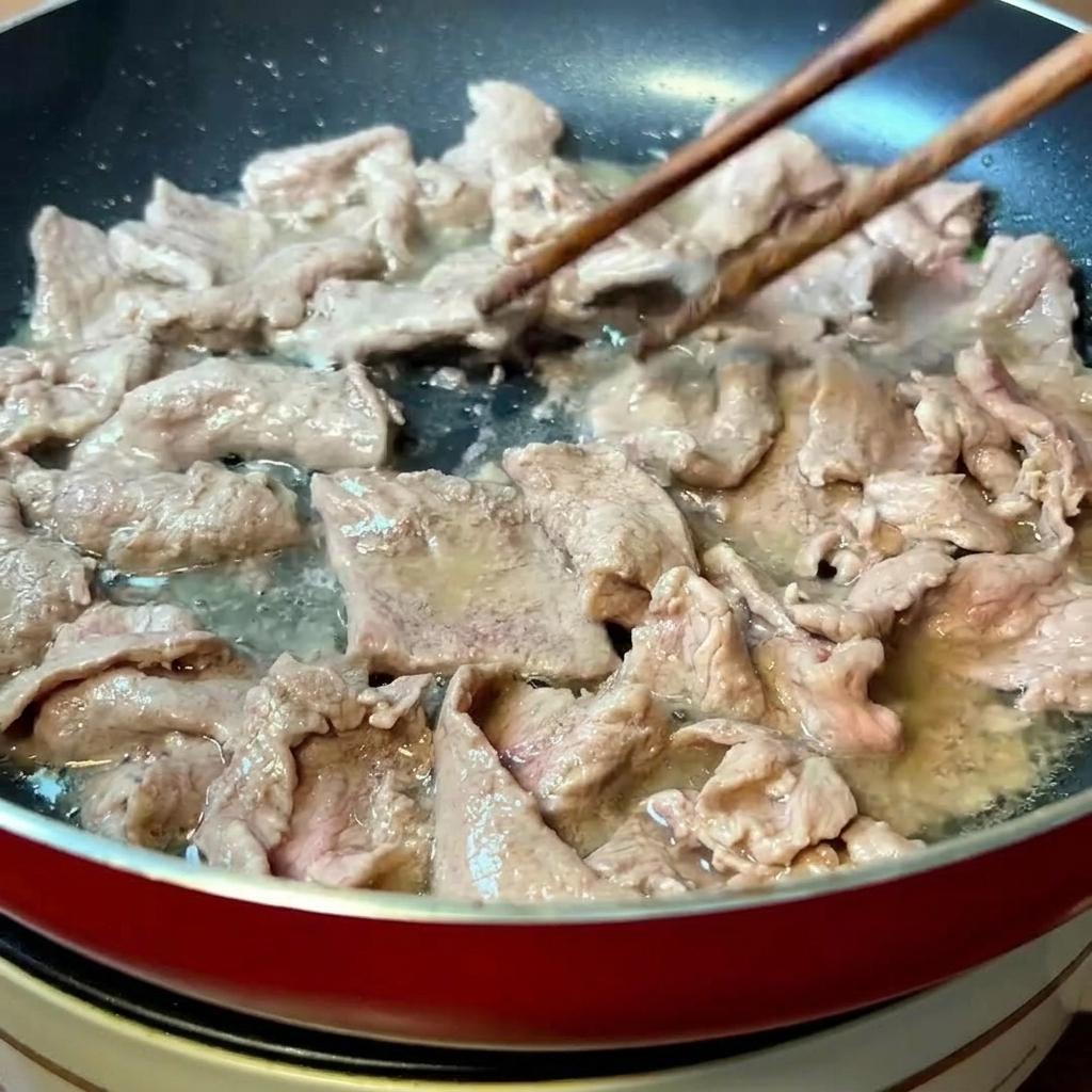 Láminas de ternera marinada salteándose con palillos en una sartén caliente hasta que cambian de color.