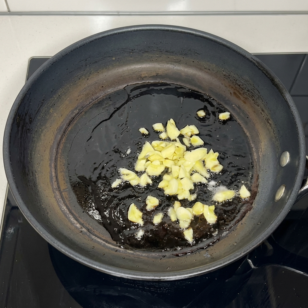 Ajo picado chisporroteando en aceite caliente dentro de una sartén oscura.