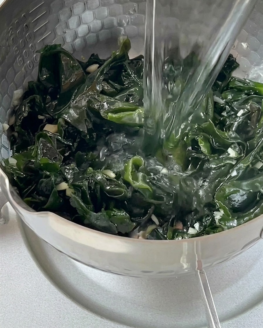 Agua hirviendo cayendo desde un hervidor de cristal sobre el wakame en una olla.