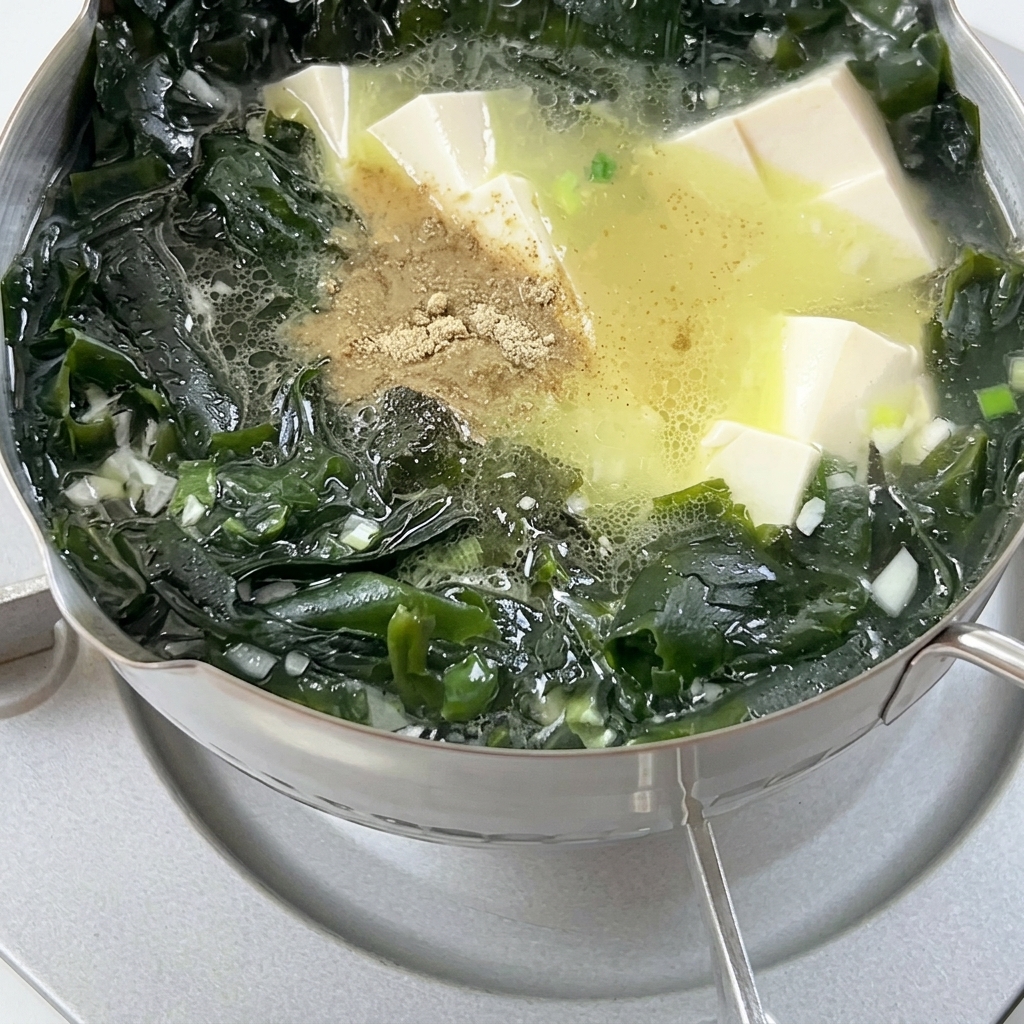 Pimienta en polvo espolvoreándose en una olla de sopa hirviendo con algas wakame y dados de tofu.