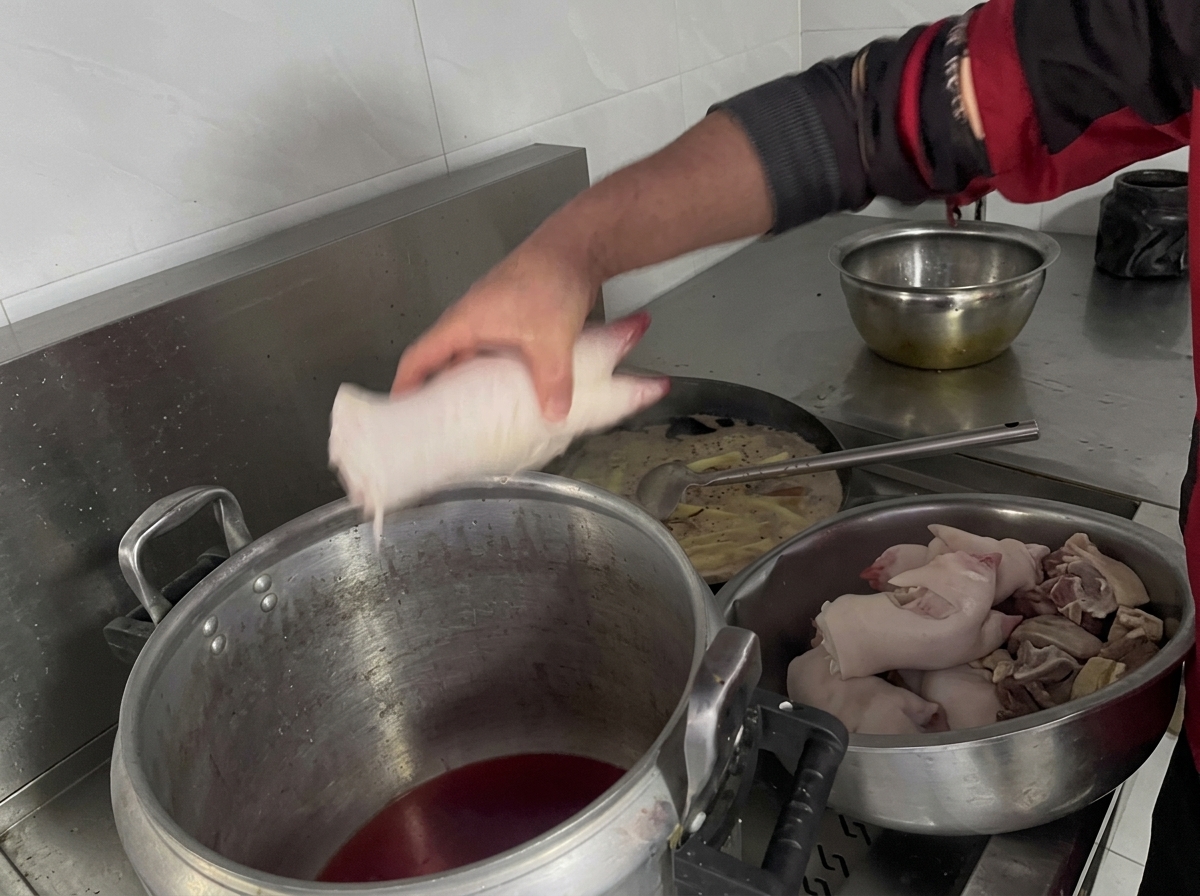 Mano colocando manitas de cerdo en una olla con líquido oscuro.