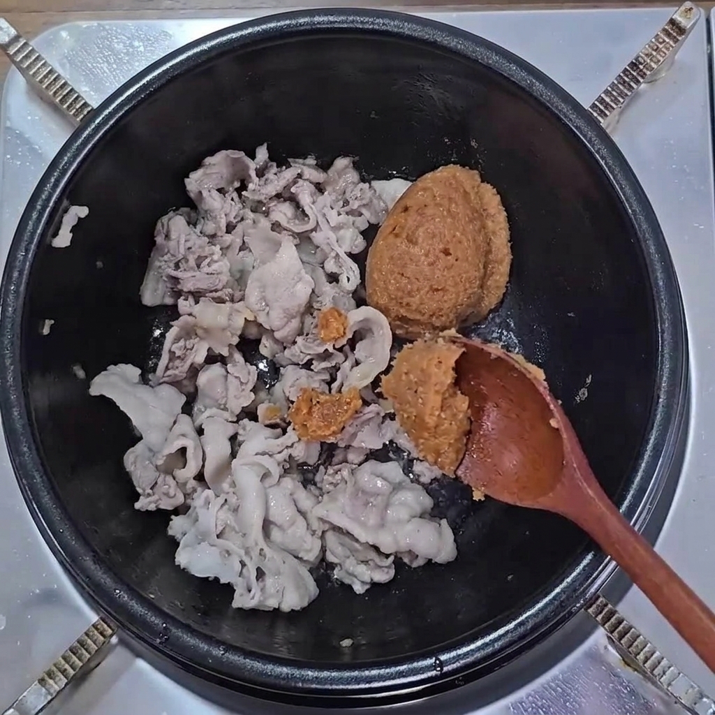 Cucharadas de pasta de soja marrón y ssamjang añadidas sobre la panceta cocinada.