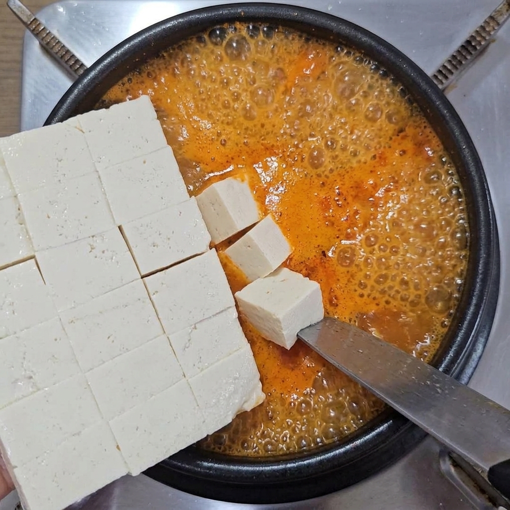 Cubos de tofu suave deslizándose desde un cuchillo hacia el interior del estofado.