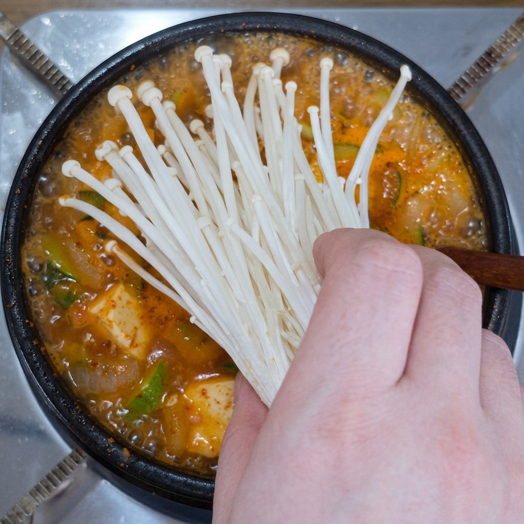 Mano colocando un manojo de setas enoki frescas en el estofado hirviendo.