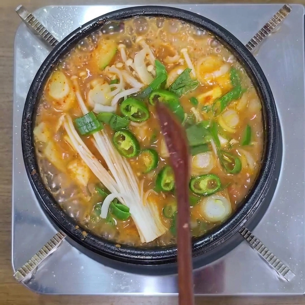 Chiles verdes, setas enoki y cebolleta hirviendo en una olla de estofado coreano.