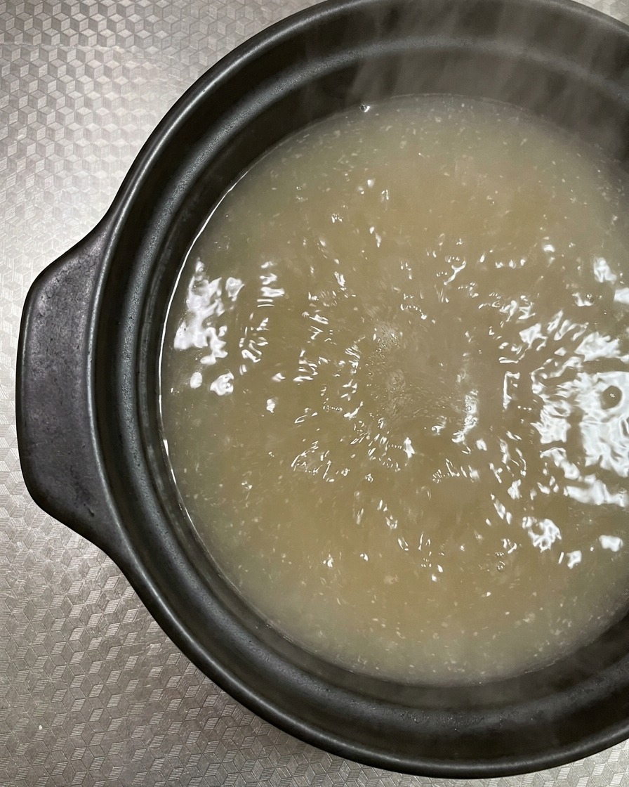 Láminas de panceta cruda siendo colocadas en el caldo hirviendo.