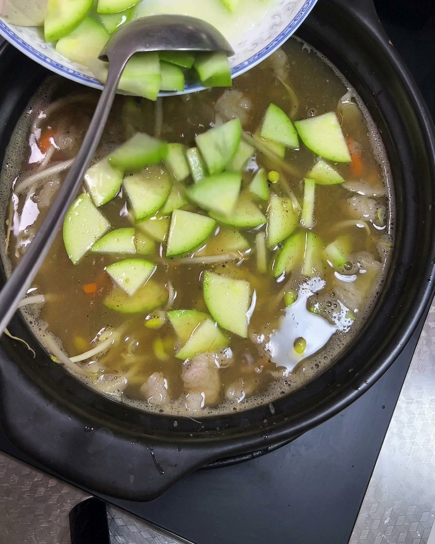 Cubos de tofu y rodajas de calabacín siendo añadidos a la olla.