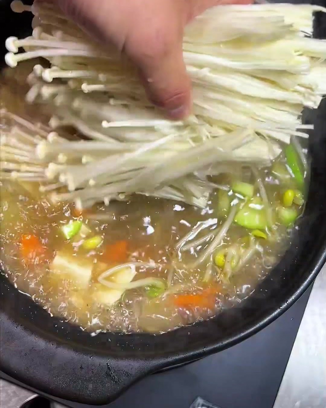 Un manojo de setas enoki siendo añadido a la olla.