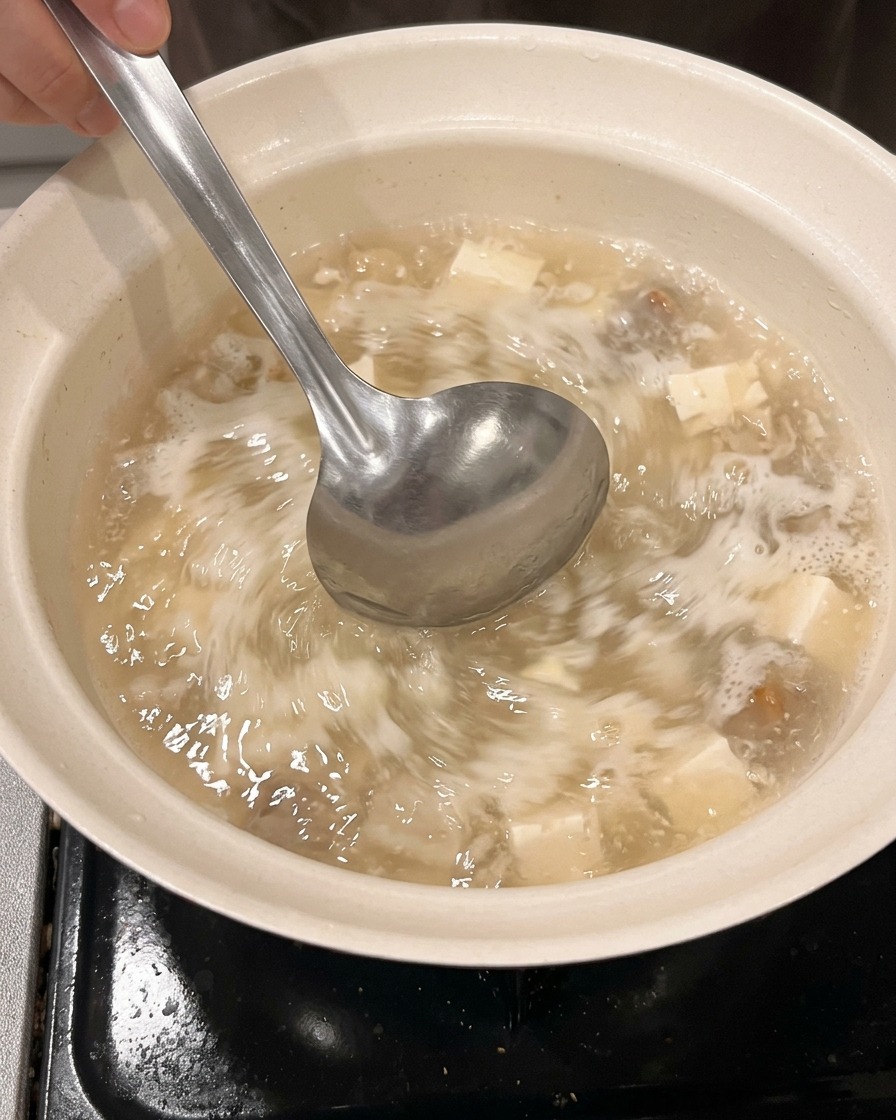 Agua y sake siendo vertidos en una olla limpia desde una taza medidora.
