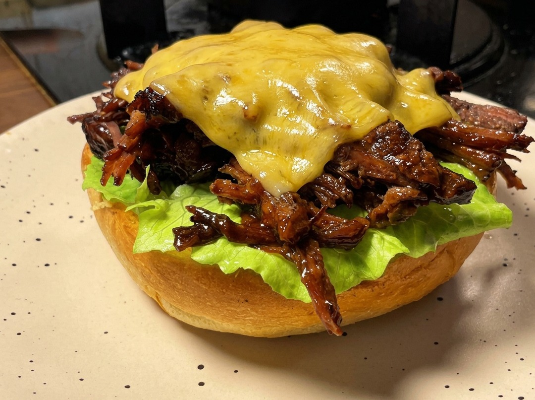 Una hamburguesa de carne deshebrada cubierta con una rebanada de queso que se está derritiendo con un soplete de cocina de mano.