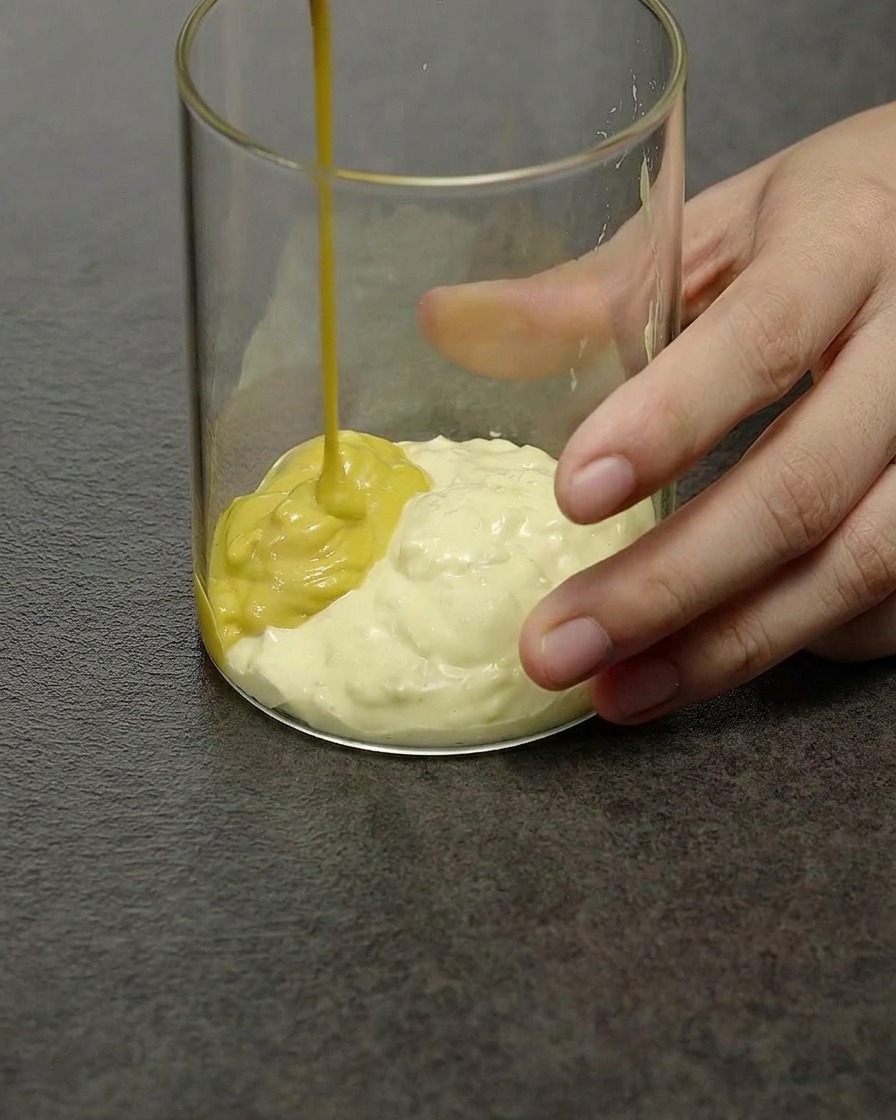 Una salsa de hamburguesa cremosa de color amarillo pálido removiéndose en un recipiente de cristal transparente.