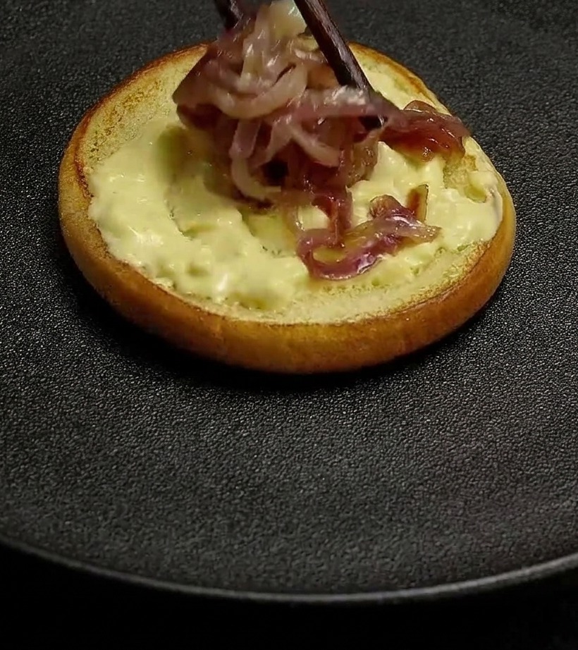 Cebollas moradas cocinadas colocándose con palillos sobre un pan untado con salsa cremosa.