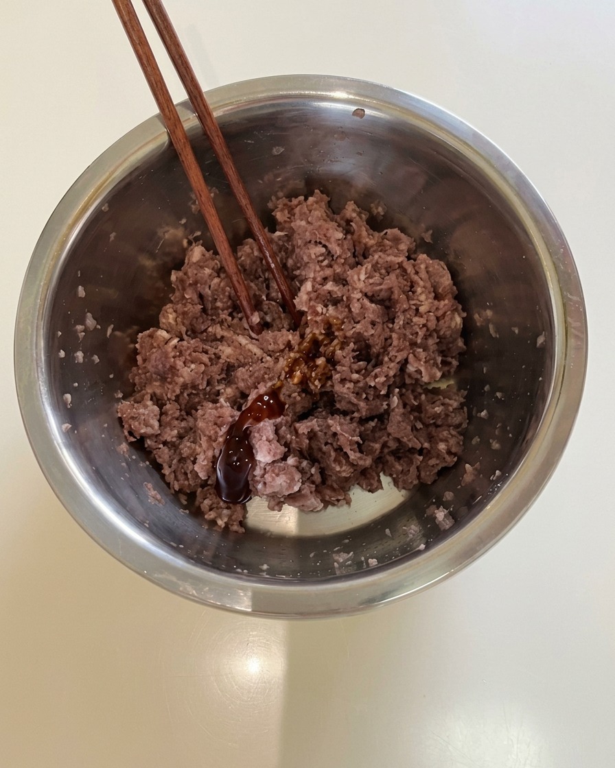 Palillos reposando en un bol de metal con carne picada sazonada y salsa oscura.
