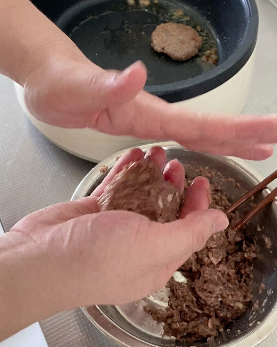 Dos manos lanzando y dando forma redonda a una bola de carne picada cruda.