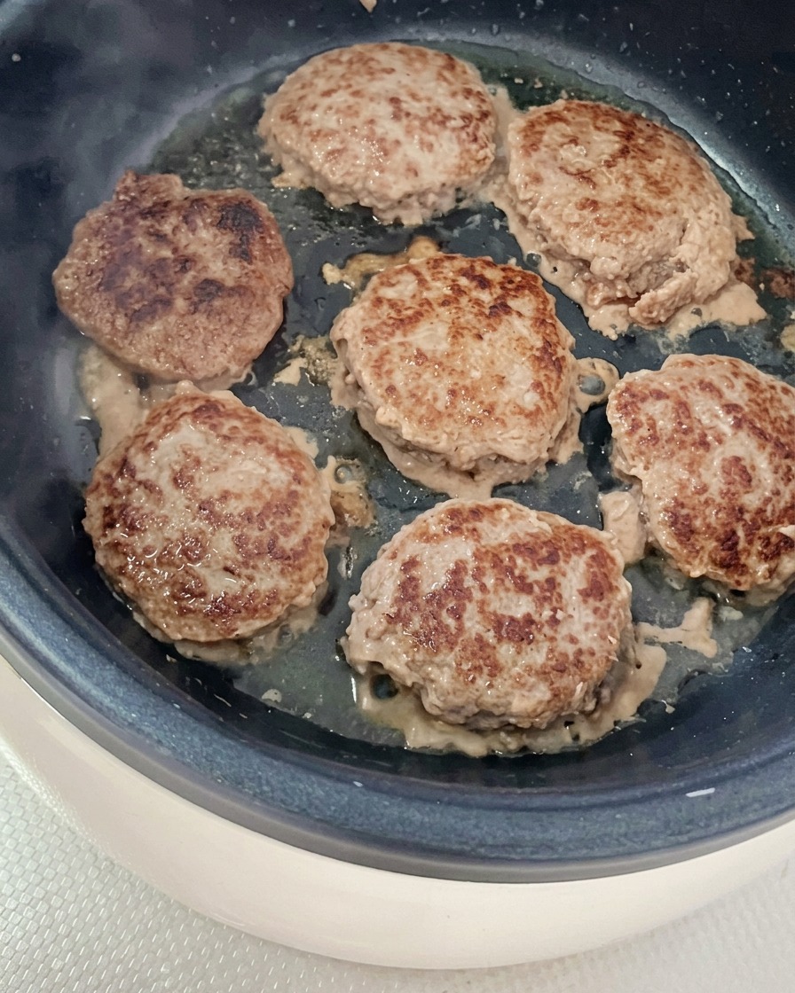 Seis hamburguesas de carne dorándose en una sartén ligeramente engrasada.