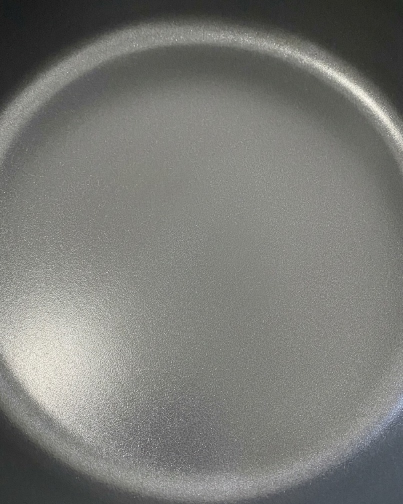 Dos rebanadas de queso cheddar derritiéndose maravillosamente sobre la carne de hamburguesa en una sartén oscura.