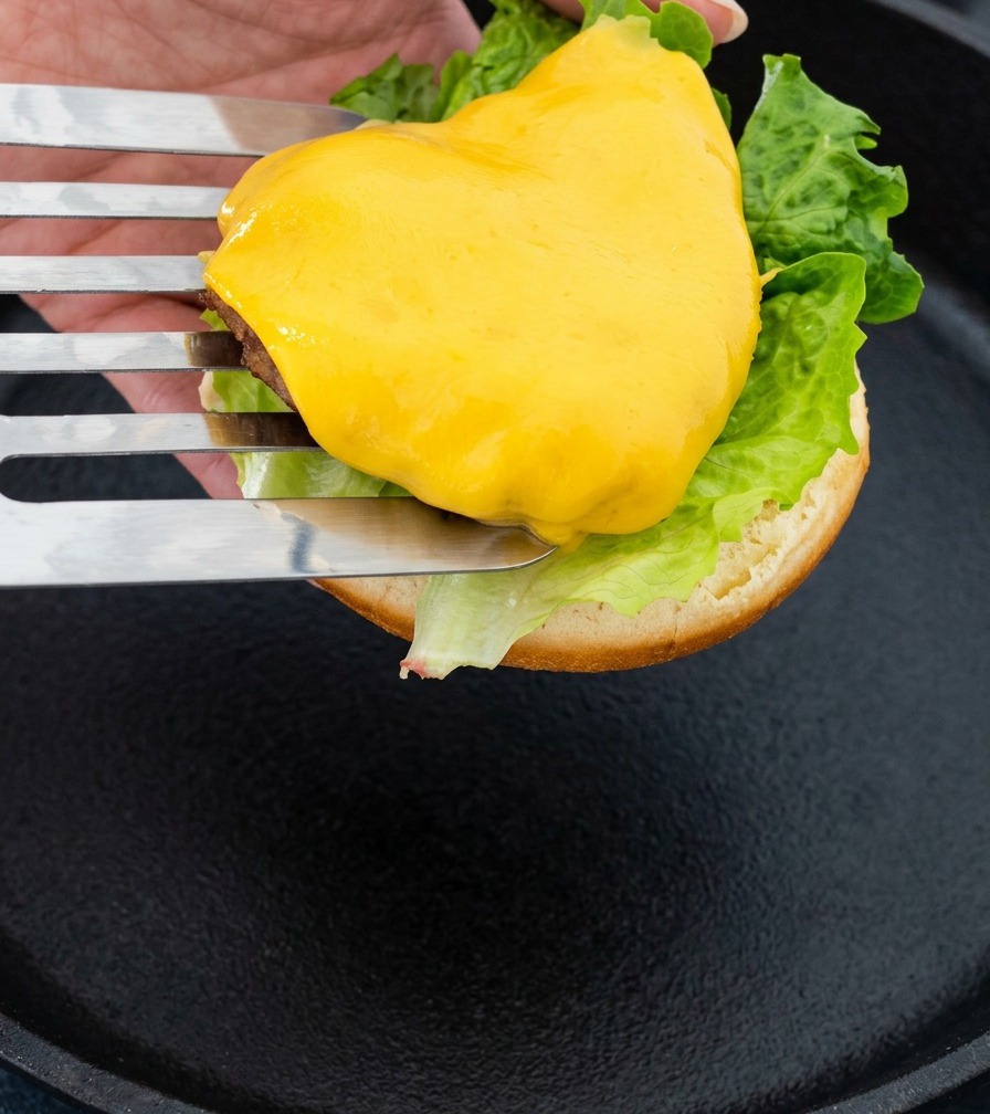 Una espátula de metal levantando la carne con queso para colocarla en la base del pan.