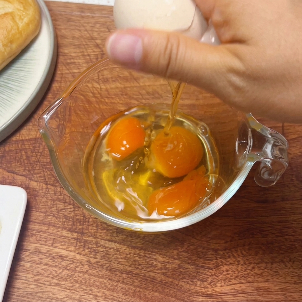Tres huevos crudos en una taza medidora de vidrio siendo batidos con palillos.