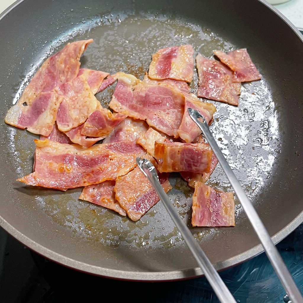 Huevos batidos cocinándose en una sartén con trozos de tocino.