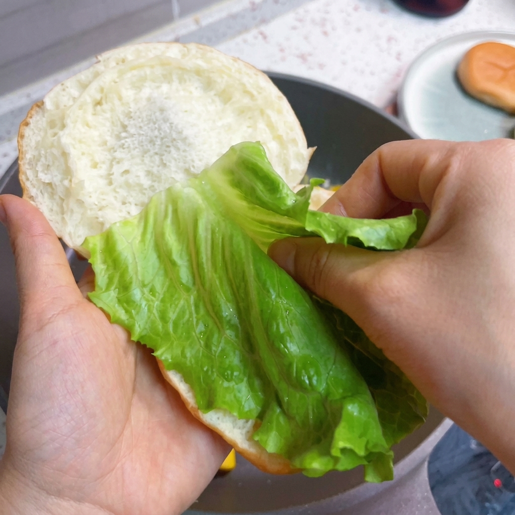 Montaje de la hamburguesa con lechuga fresca, tocino y huevos esponjosos sobre un pan.