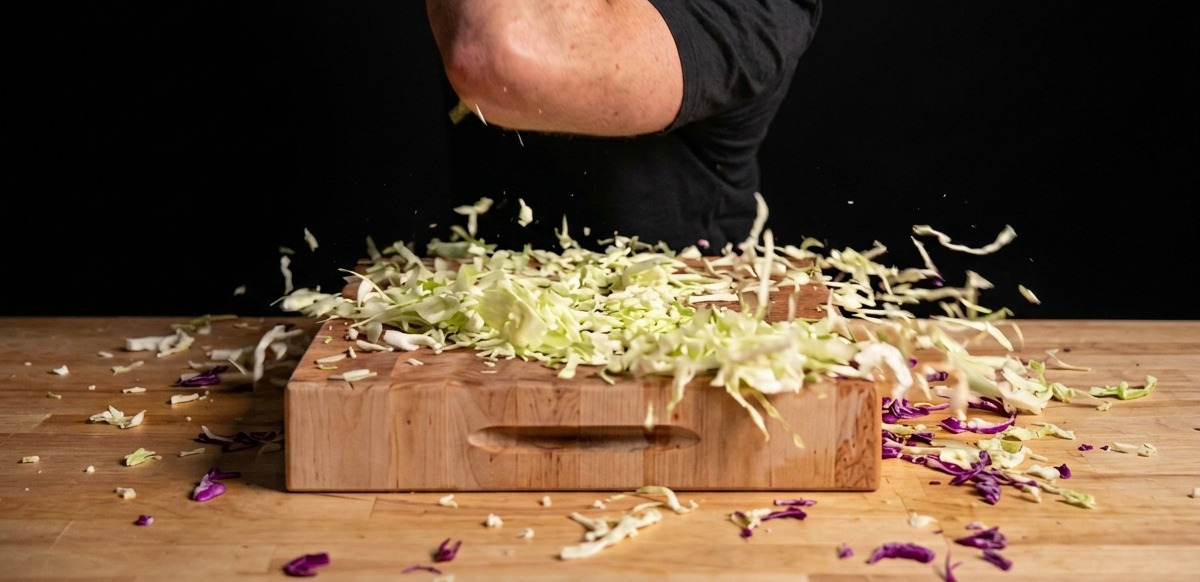 Repollo verde y morado siendo picado finamente sobre una tabla de madera.