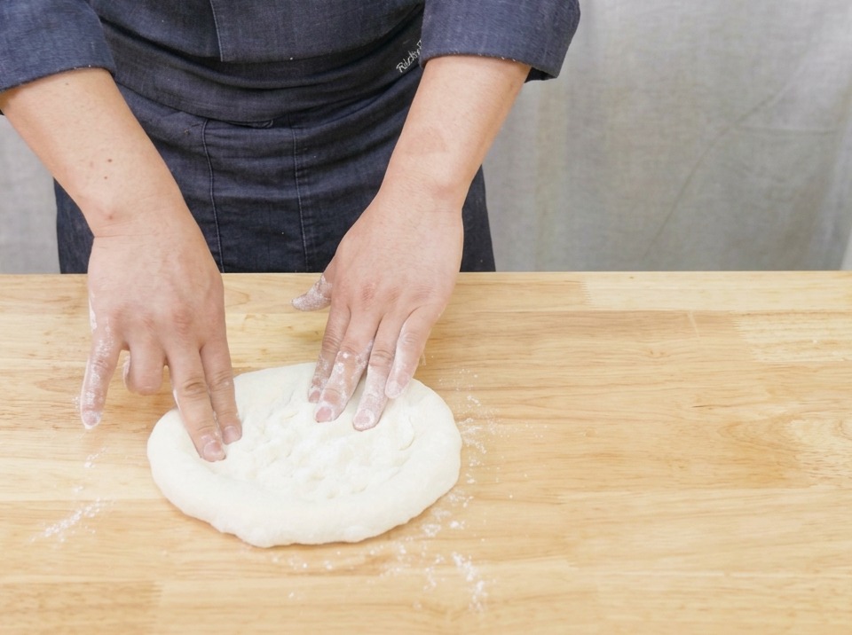 Primer plano de unas manos estirando y dando forma suavemente a una masa redonda de pizza sobre una tabla de madera.