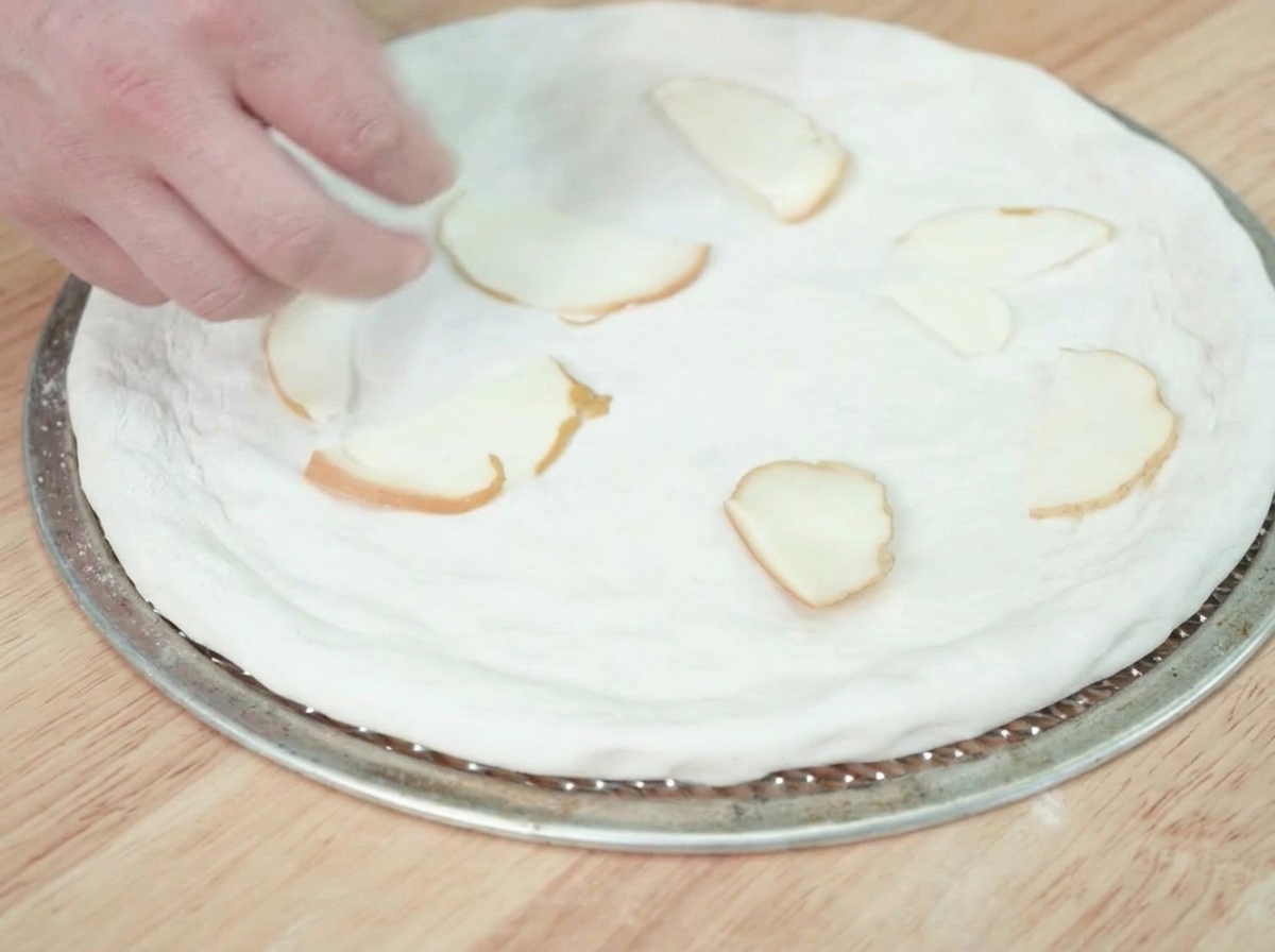 Rebanadas de queso ahumado que se colocan sobre la base de masa de pizza cruda.