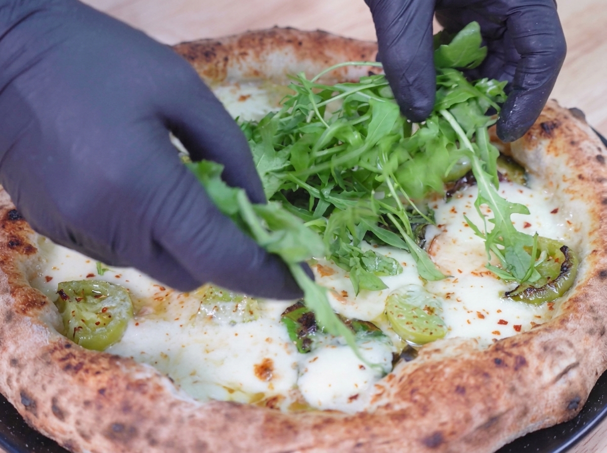 Hojas verdes y frescas de rúcula que se colocan encima de una pizza horneada y burbujeante.