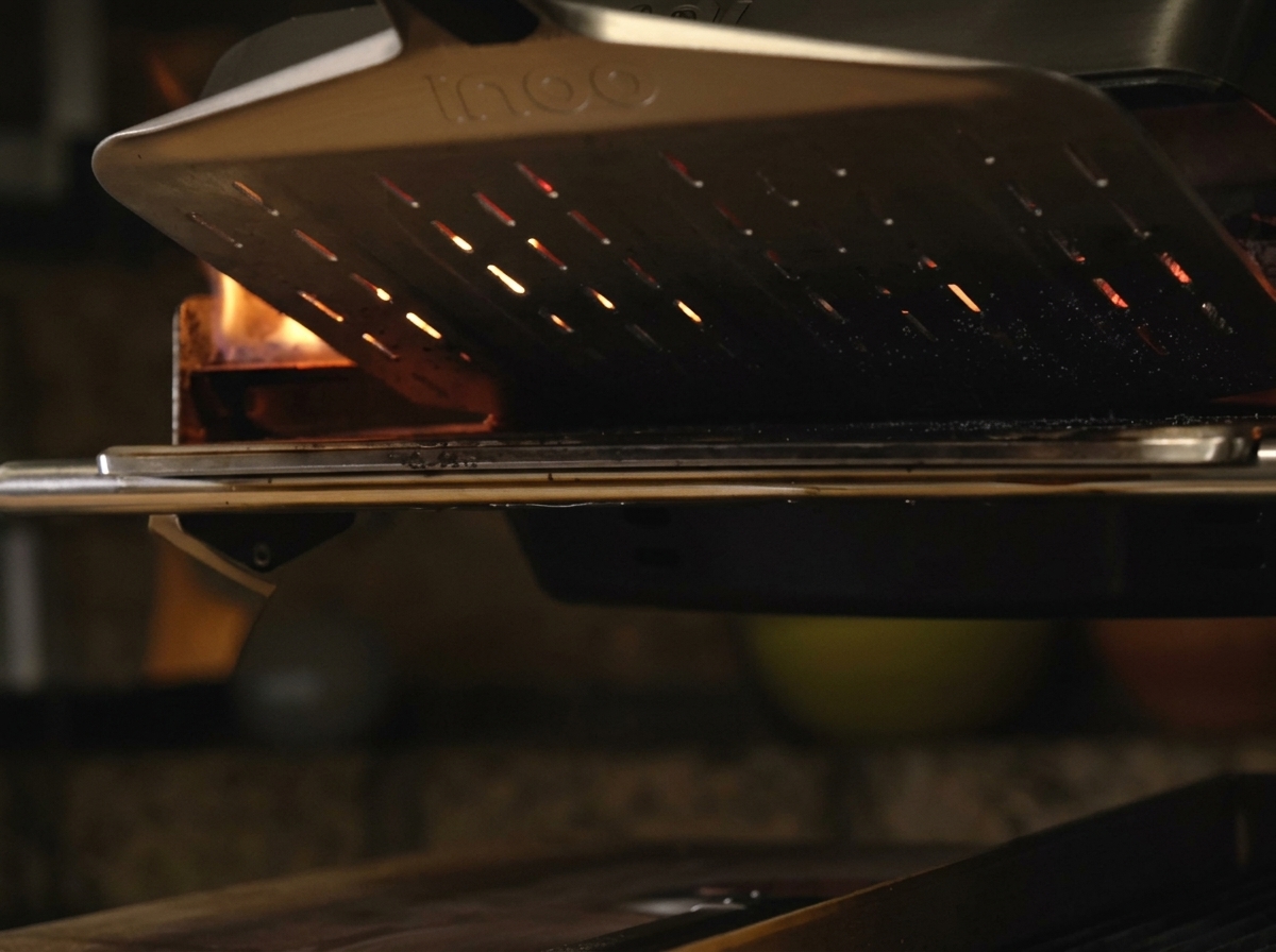 Pizza sobre una pala de metal deslizándose en un horno portátil muy caliente con llamas naranjas en el fondo.