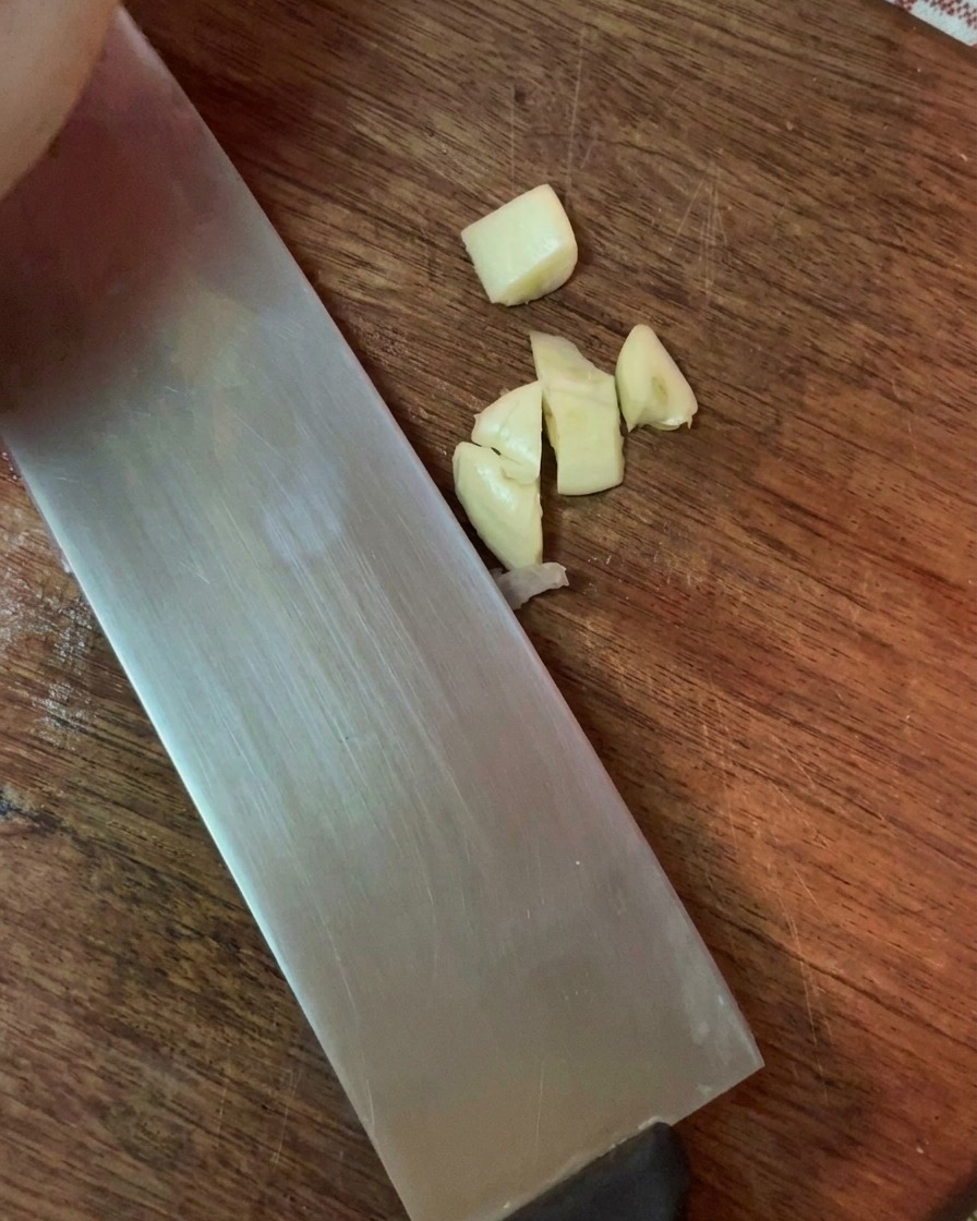 Dientes de ajo picados finamente junto a la hoja de un cuchillo en una tabla de madera.