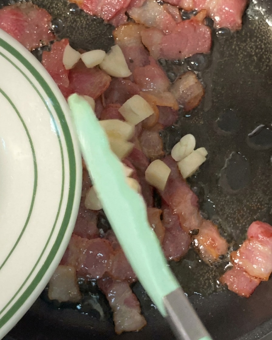 Ajo picado siendo añadido a una sartén con tocino crujiente.