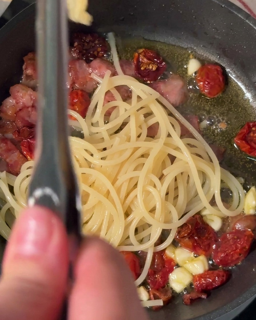 Transfiriendo espagueti cocido directamente a una sartén caliente con ingredientes.