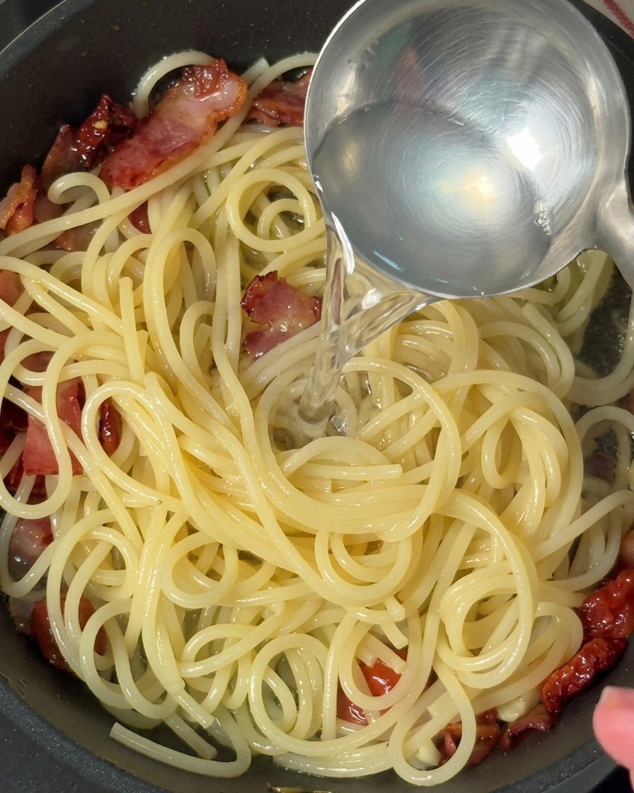 Un cucharón vertiendo agua de cocción en una sartén con pasta.