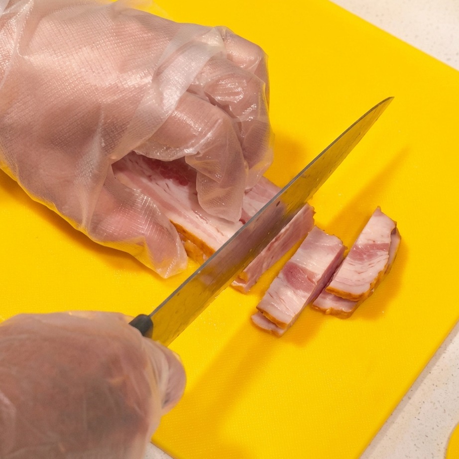 Tiras de tocino crudo cortándose sobre una tabla de cortar amarilla.