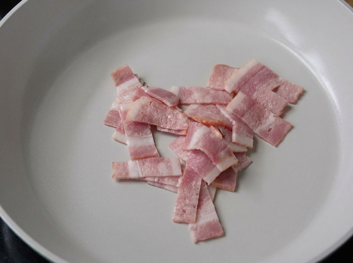 Tiras de bacon friéndose en una sartén.