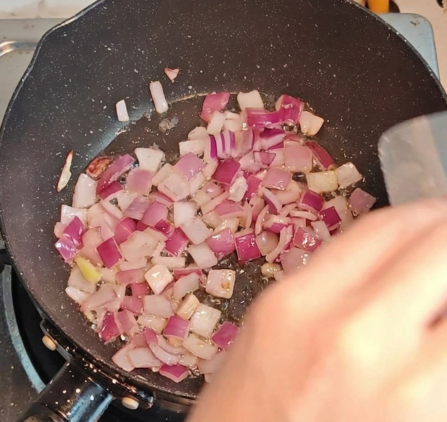 Bacon picado y cebollas friéndose juntos en una sartén a fuego fuerte.