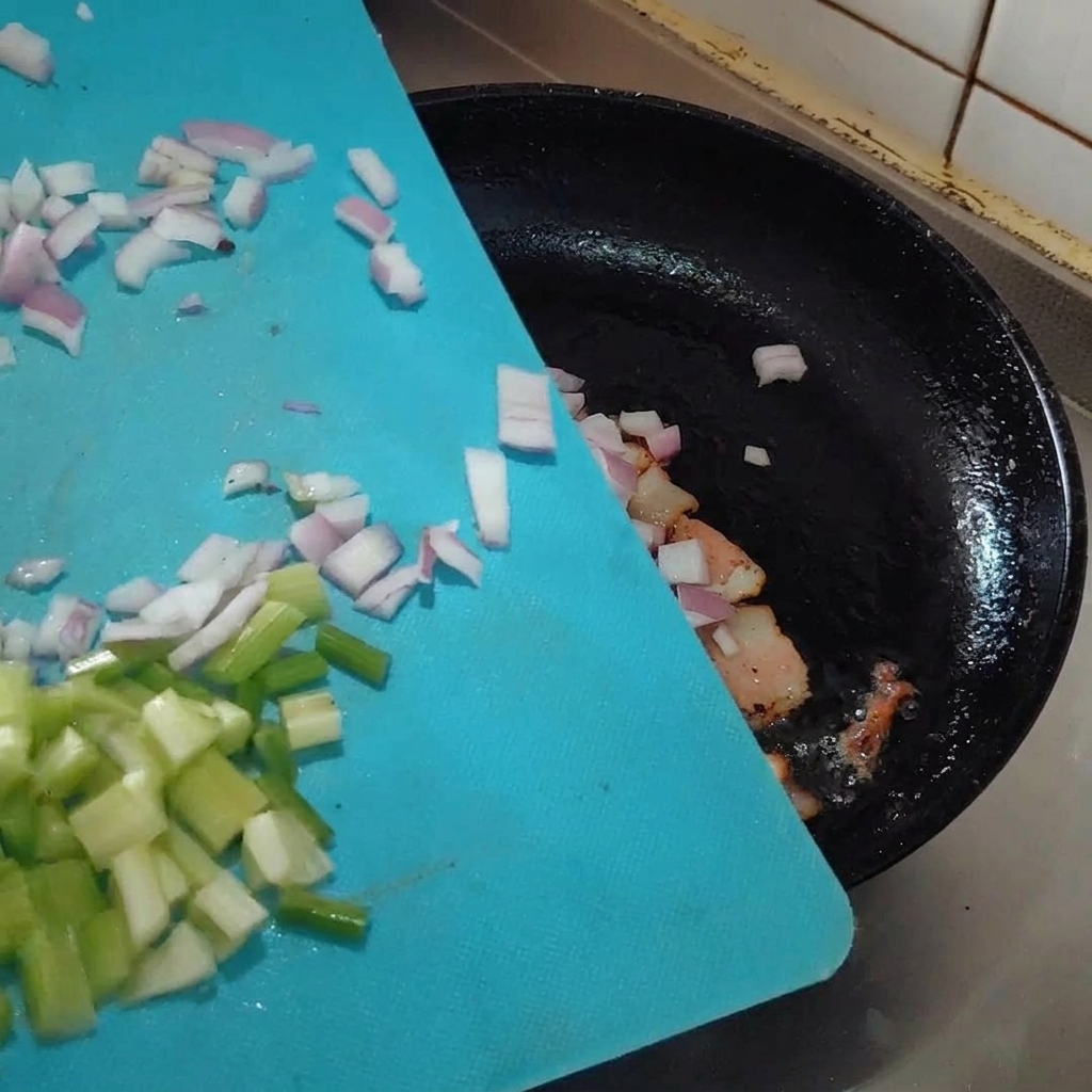Aromáticos picados siendo añadidos a la sartén con el tocino.