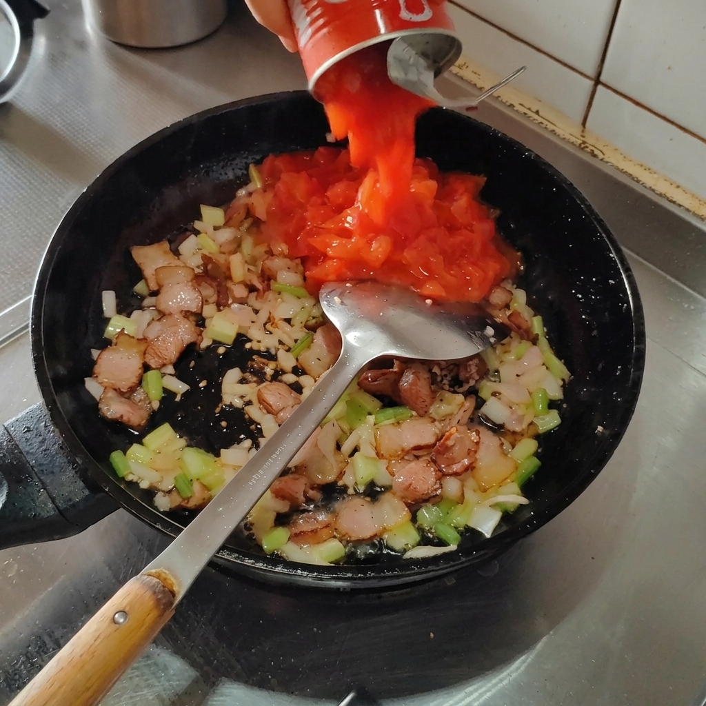 Tomates enlatados vertiéndose en la sartén sobre la mezcla de tocino y aromáticos.