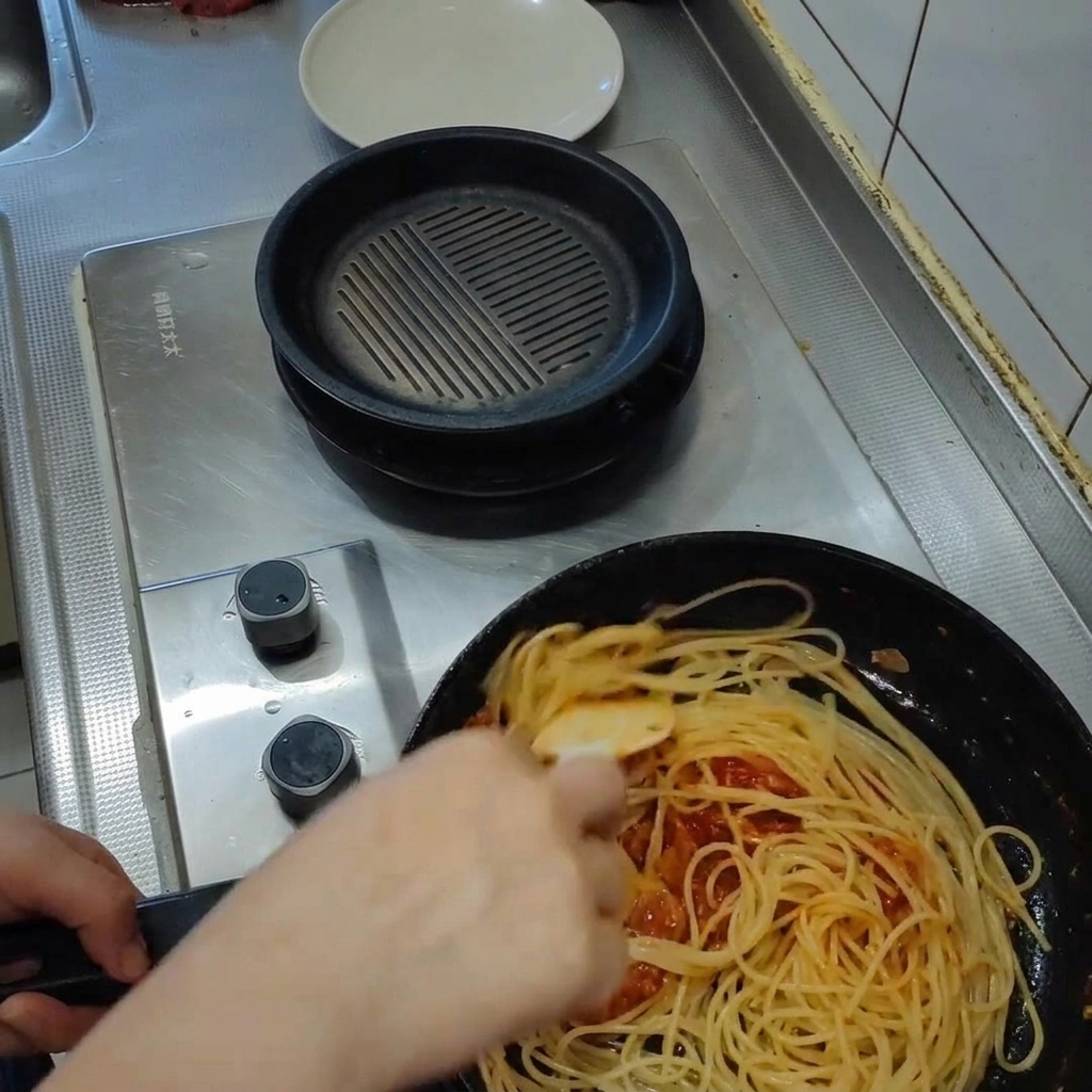 Pasta salteándose en una rica salsa de tomate dentro de una sartén, con vapor elevándose mientras la salsa se emulsiona.
