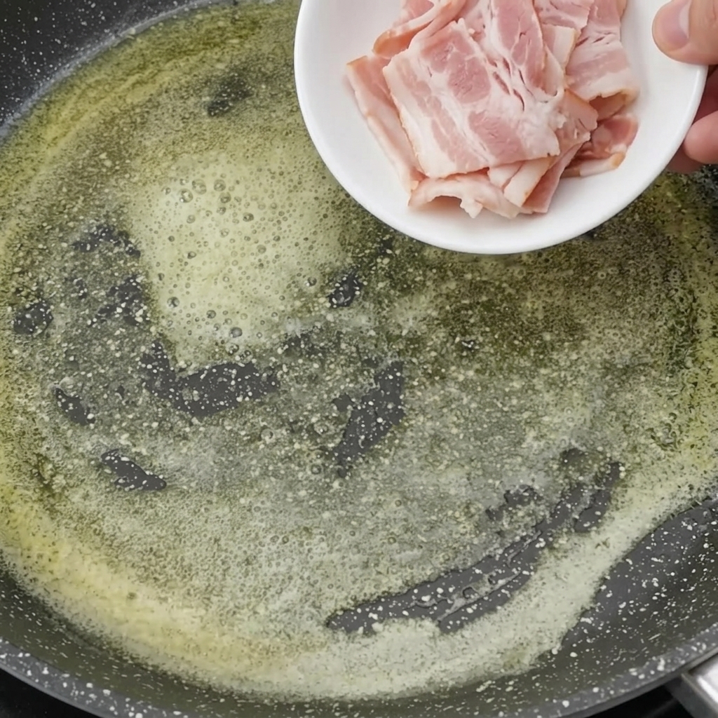 Trozos de bacon friéndose en la mantequilla hasta quedar dorados.