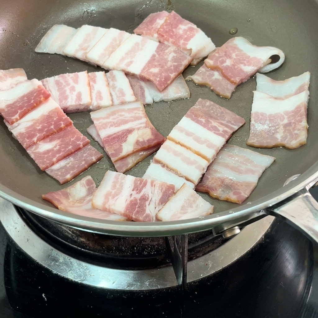 Tiras de bacon crujiente friéndose en una sartén.