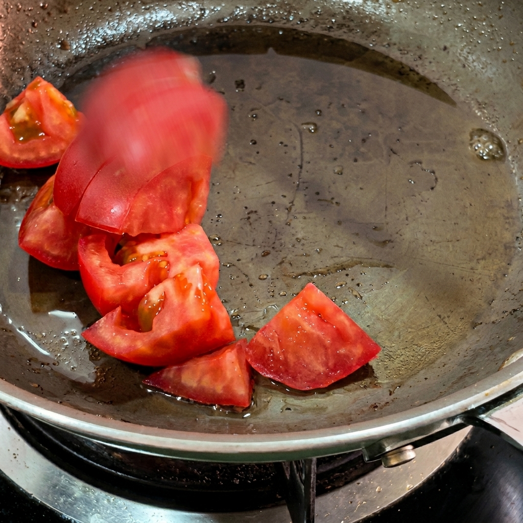 Trozos de tomate ablandándose en la grasa del bacon dentro de una sartén.